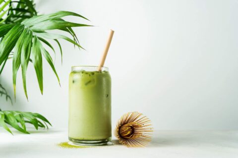 japansk isad matcha latte med bambusugrör i glas på vit bakgrund.
